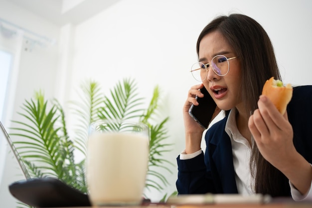 Une femme d'affaires occupée et fatiguée mangeant du pain et du lait pour le déjeuner au bureau et travaillant pour livrer des états financiers à un patron Overworked et malsain pour les repas prêts concept de burn-out