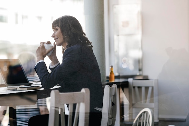 Femme d'affaires avec ordinateur portable, assise dans un café, buvant du café