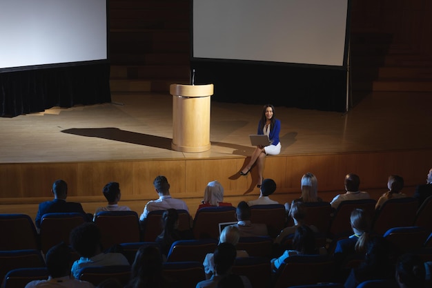 Une femme d'affaires avec un ordinateur portable assise sur scène dans l'auditorium