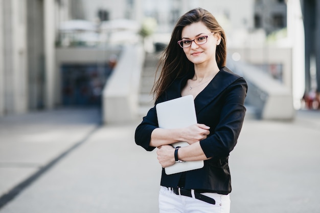 Femme d&#39;affaires avec un ordinateur portable debout dans une rue dans une ville moderne