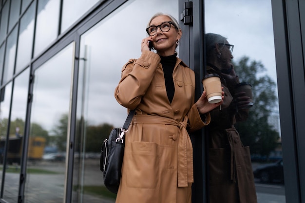 Femme d'affaires parlant au téléphone entre dans l'immeuble de bureaux avec une tasse de café