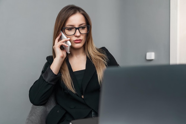 Femme d'affaires parlant au téléphone portable au bureau et regardant un ordinateur portable