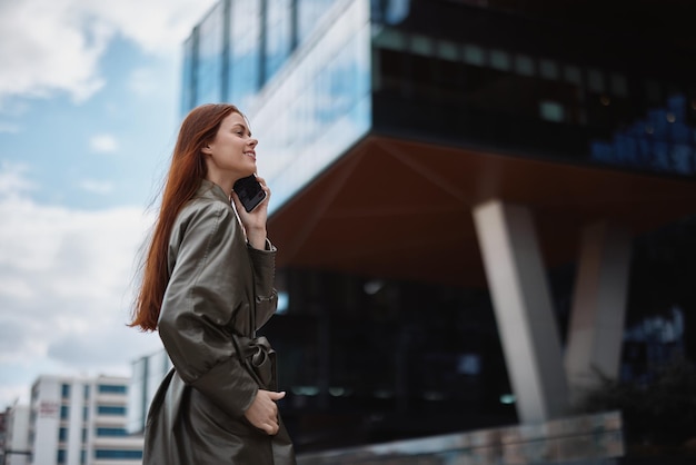 Femme d'affaires parlant au téléphone et souriant avec les dents dans le contexte de la technologie des bâtiments de la ville et du concept de développement commercial en ligne