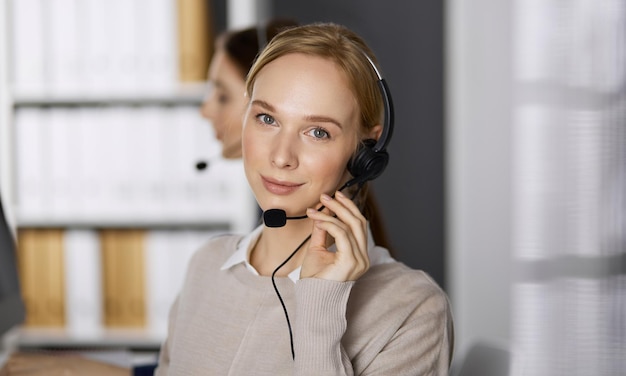 Femme d'affaires parlant par casque alors qu'il était assis au bureau. Centre d'appels et groupe de personnes diverses dans les affaires.