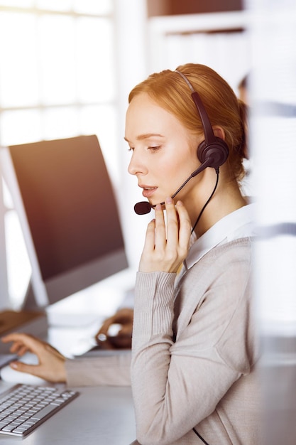 Femme d'affaires parlant par casque dans un bureau ensoleillé. Centre d'appels et groupe de personnes diverses dans les affaires.