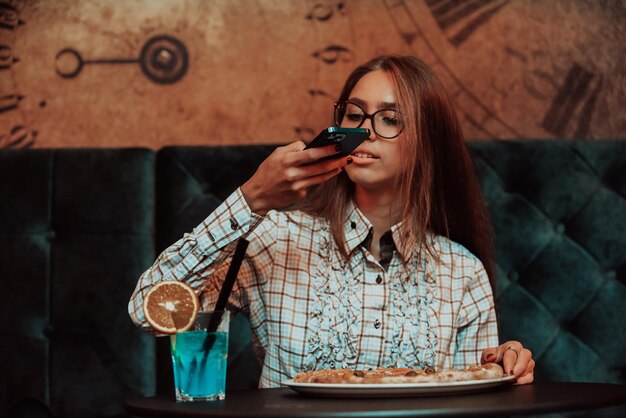 Une femme d'affaires en pause déjeuner photographie une pizza dans un restaurant moderne Mise au point sélective