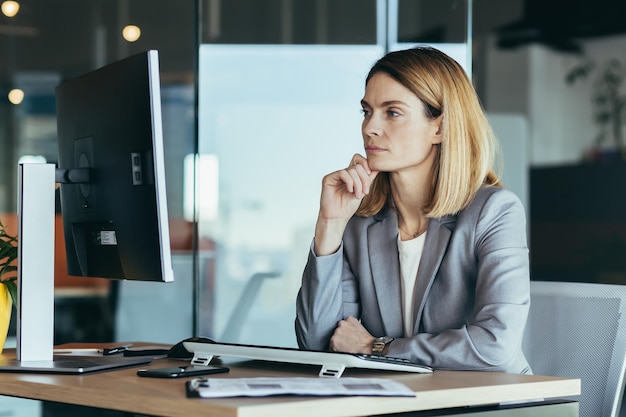 Femme d'affaires pensante regardant un moniteur d'ordinateur femme d'affaires travaillant dans un bureau moderne planifiant un nouveau projet et une stratégie commerciale