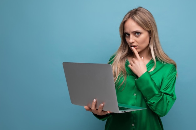 Femme d'affaires pigiste pensant au travail tenant un ordinateur portable dans ses mains sur un bleu vif