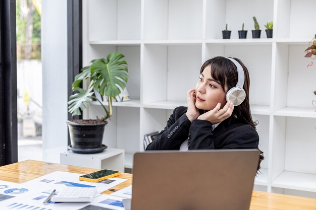 Femme d'affaires portant des écouteurs écoutant de la musique dans son bureau, elle se repose en écoutant de la musique, elle devient émue par la musique et danse sur la musique. L'idée relaxante au travail.