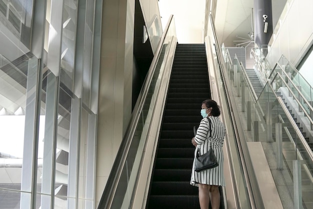 Femme d'affaires portant un masque facial debout sur un escalator