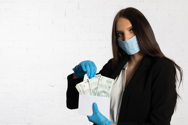 Une femme d'affaires portant un masque et des gants de protection met un paquet de billets de banque dans l'enveloppe