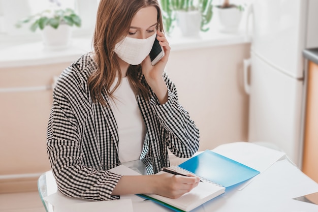 Femme d'affaires portant un masque médical de protection est isolée à la maison et appelle au téléphone, travaille, recherche d'emploi, études. Jeune fille, chercher, éloigné, éloigné, travail, sur, quarantaine,