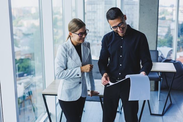 Femme d'affaires positive debout avec un collègue caucasien parlant à un homme d'affaires au bureau Relations d'affaires entre collègues souriants dans une atmosphère chaleureuse