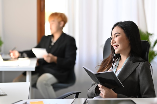 Femme d'affaires positive tenant un livre et travaillant dans un bureau moderne.