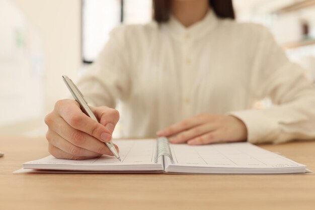 Femme d'affaires prend des notes dans l'organisateur à table dans le bureau gros plan d'une femme gestionnaire avec un stylo