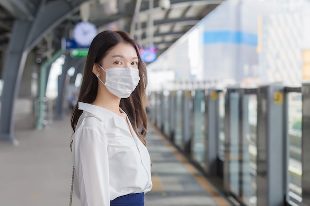 Une femme d'affaires professionnelle asiatique aux cheveux longs porte un masque attend d'aller au bureau du lieu de travail