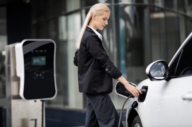 Une femme d'affaires progressiste branche la prise du chargeur de la station de charge à l'EV