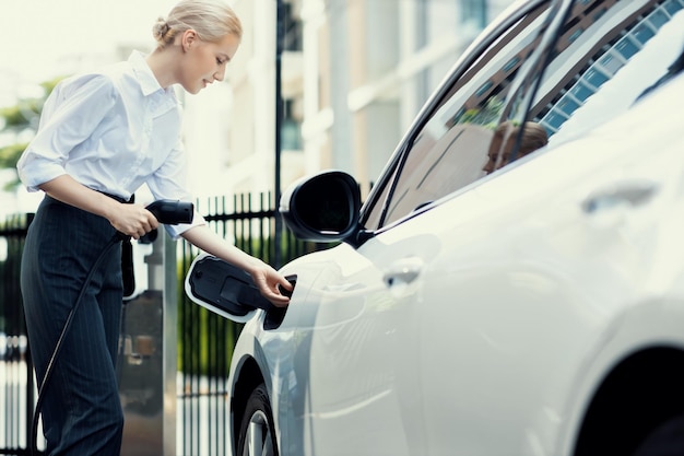 Une femme d'affaires progressiste branche la prise du chargeur de la station de charge à l'EV