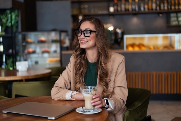 Femme d'affaires propriétaire de restaurant utiliser un ordinateur portable dans les mains vêtu d'un tailleur-pantalon élégant assis à table dans un restaurant avec un fond de comptoir de bar