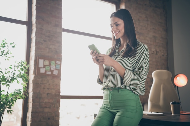 Femme d'affaires prospère à l'aide de téléphone portable au loft industriel moderne