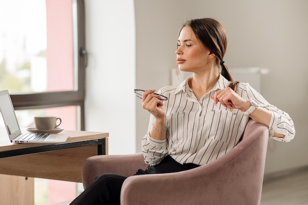 Femme d'affaires prospère en chemise portant des lunettes travaillant avec un ordinateur portable au bureau