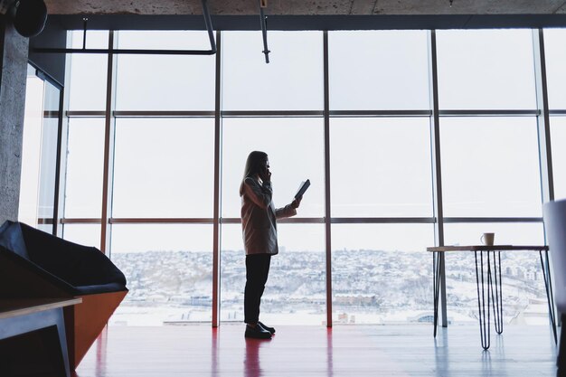 Femme d'affaires prospère, debout, regardant par la fenêtre, profitant de la vue sur la ville, confiante, riche, dirigeante, pensant au succès de l'entreprise et à la vision de l'avenir, planifiant de nouveaux objectifs