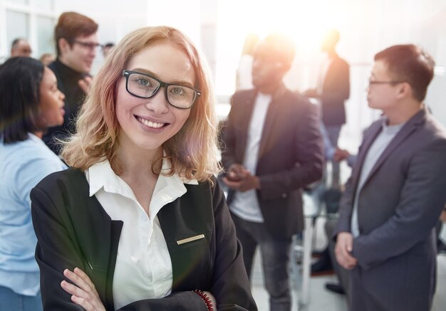 Femme d'affaires prospère debout avec son personnel en arrière-plan dans un bureau moderne et lumineux