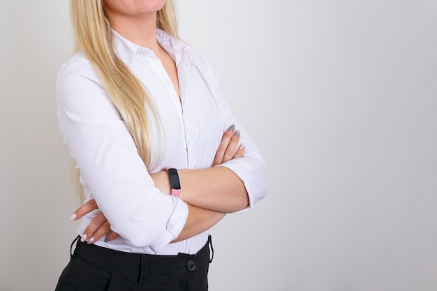 Femme d'affaires prospère avec les mains jointes sans visage, chemise blanche sur mur clair