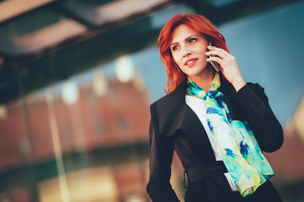 Femme d'affaires prospère souriante parlant sur smartphone dans le quartier des bureaux.