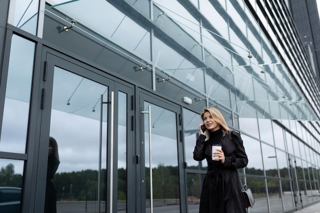 Femme d'affaires prospère va travailler au bureau avec un verre de café par téléphone portable