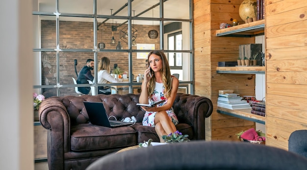 Photo une femme d'affaires qui travaille avec un ordinateur portable en train de parler au téléphone assise sur le canapé dans le bureau