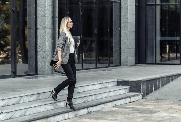 Une femme d'affaires quitte l'immeuble de bureaux avec un dossier dans les mains. Travailleur de bureau. Jeune femme en tailleur