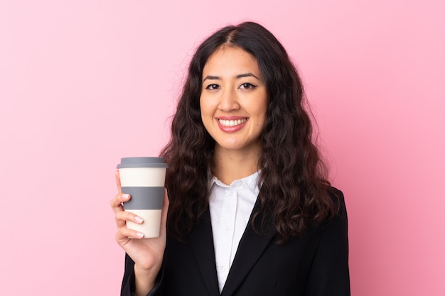 Femme d'affaires de race mixte tenant du café à emporter sur le mur rose isolé