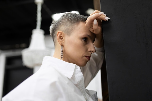 Femme d'affaires réfléchie dans une chemise blanche avec une coupe de cheveux courte se tient appuyée sa tête contre le