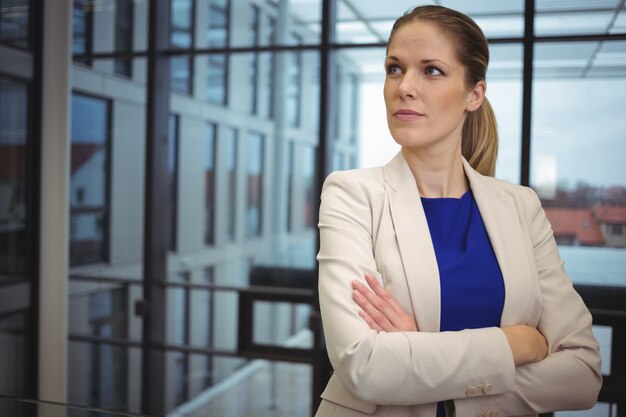 Femme d'affaires réfléchie debout avec les bras croisés dans le couloir