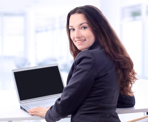 Femme d'affaires réfléchie pour un ordinateur portable au bureau avec un sourire.