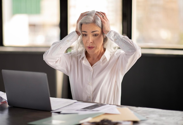 Femme d'affaires regardant un ordinateur portable touchant la tête ayant un problème au bureau