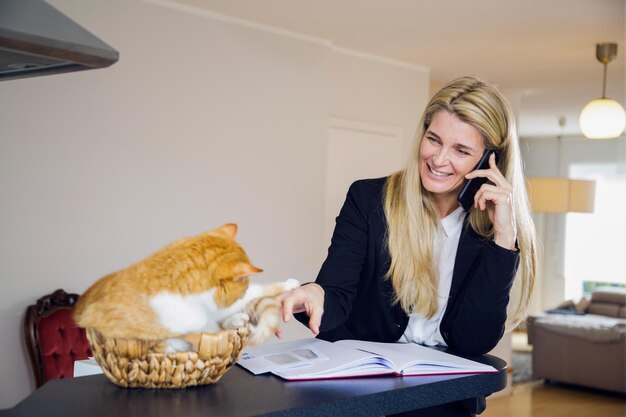 Photo une femme d'affaires répond au téléphone portable pendant que le chat est assis sur la table à la maison.