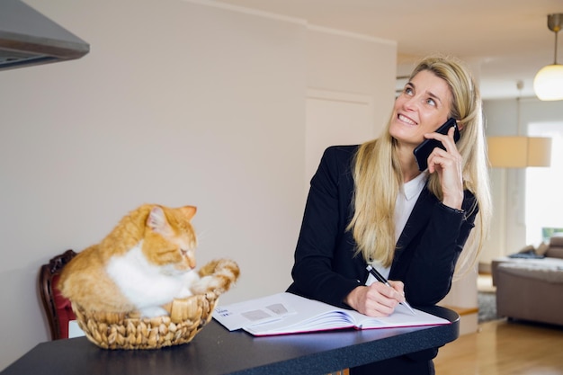 Photo une femme d'affaires répond au téléphone portable pendant que le chat est assis sur la table à la maison.