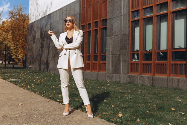 Femme d'affaires respectable en costume formel blanc et lunettes de soleil debout dans la rue de la ville