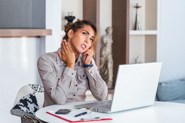 Femme d'affaires ressentant des douleurs dans le cou après s'être assis à la table avec un ordinateur portable.