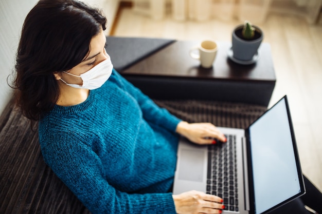 Photo la femme d'affaires reste à la maison et travaille pendant la quarantaine de l'épidémie de coronavirus. travailleuse portant un masque médical et tapant sur un ordinateur portable. concept de prévention de la propagation de la pandémie de covid-19.