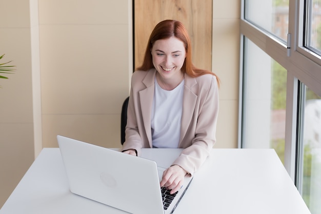 Femme d'affaires rousse heureuse et souriante travaillant à l'ordinateur assis à la maison