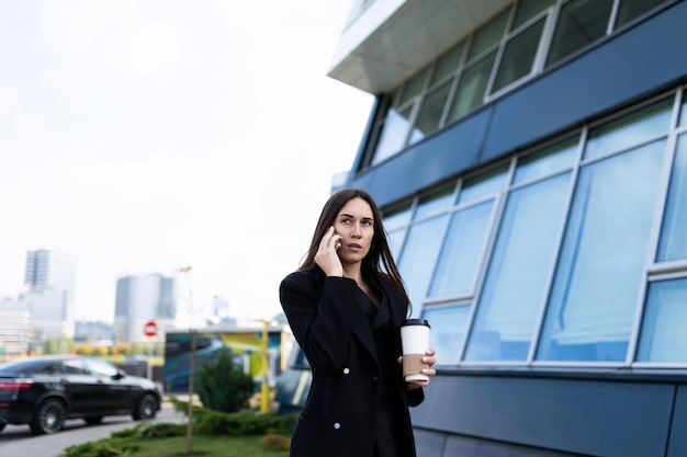 Femme d'affaires se précipitant à une réunion parlant sur un téléphone portable avec une tasse de café dans ses mains