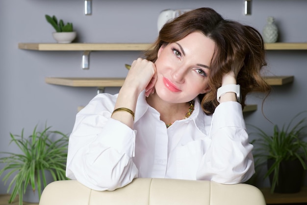 La femme d'affaires se tient dans son bureau se penchant sur une chaise et regardant l'appareil-photo