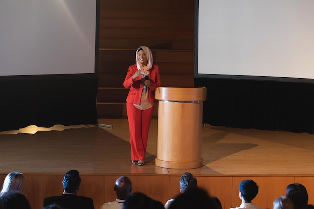 Une femme d'affaires se tient près du podium et fait une présentation à l'auditoire