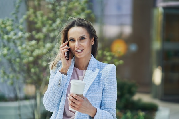 Femme D'affaires Séduisante Adulte Avec Smartphone Et Café Marchant Dans La Ville. Photo De Haute Qualité