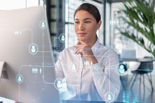 Femme d'affaires séduisante en chemise blanche sur le lieu de travail travaillant avec un ordinateur portable pour embaucher de nouveaux employés pour le conseil en affaires internationales Icônes d'hologramme de médias sociaux RH sur fond de bureau