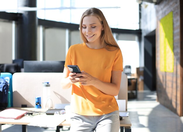 Une femme d'affaires séduisante utilise un téléphone portable alors qu'elle est assise sur le bureau.