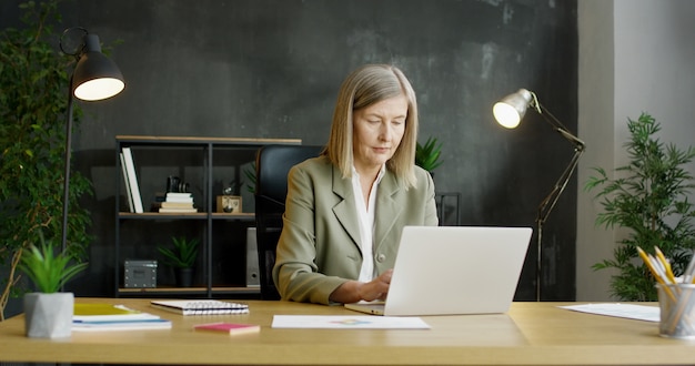 Femme d'affaires senior assis au bureau et travaillant sur ordinateur portable.